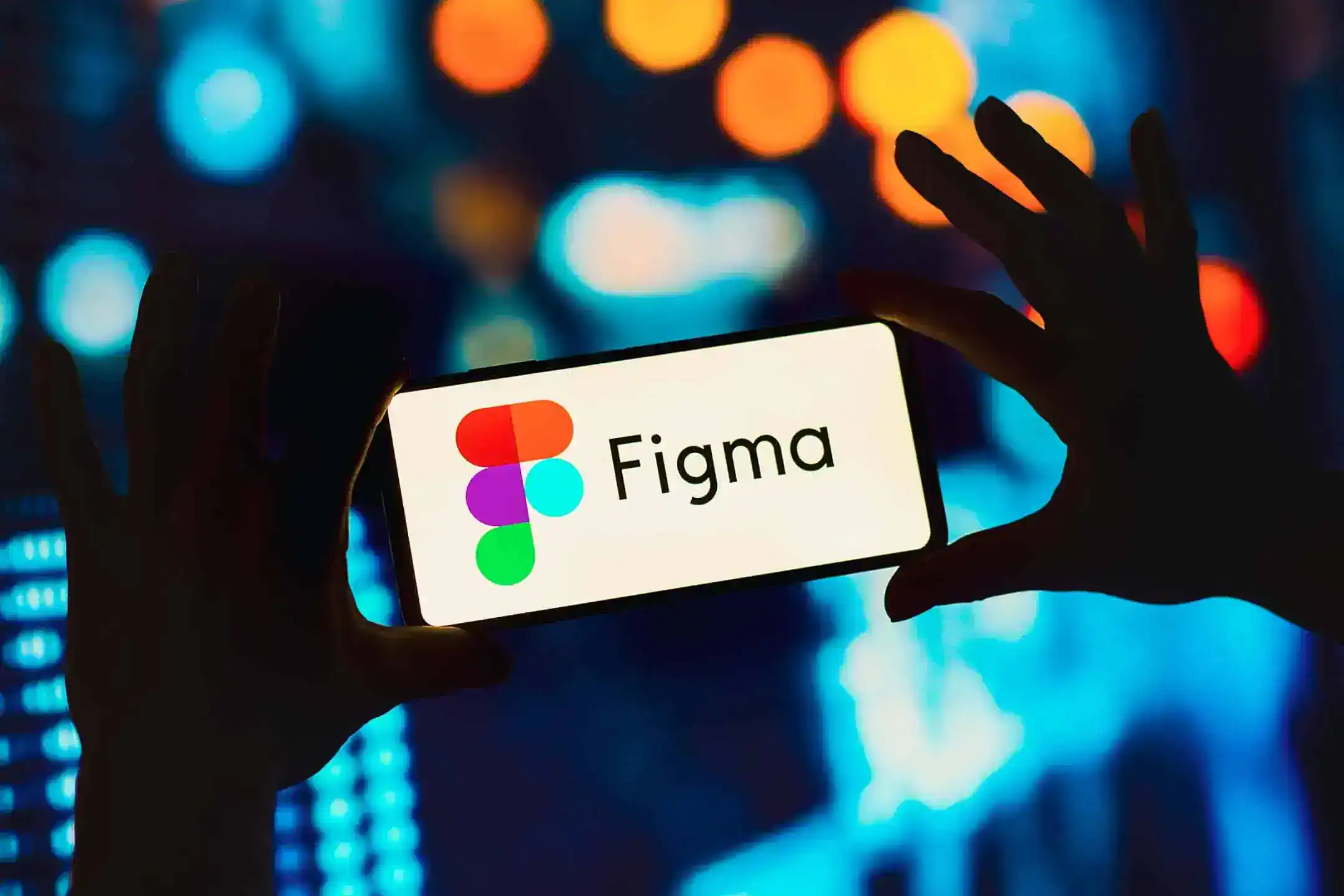 The Figma logo displayed on a smartphone screen being held up in front of blurred lights