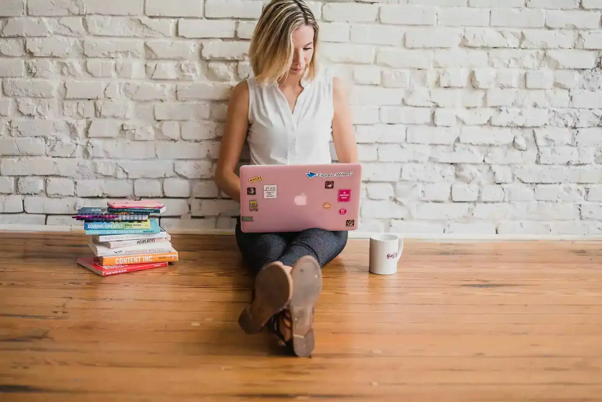 A woman sitting by a wall using her laptop